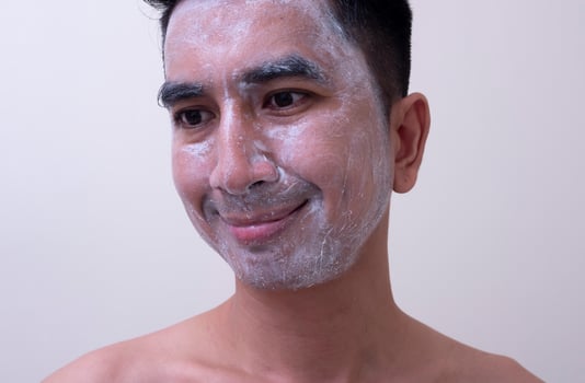 Asian handsome young man applying cream at his face with smiley face, Skin care concept photo