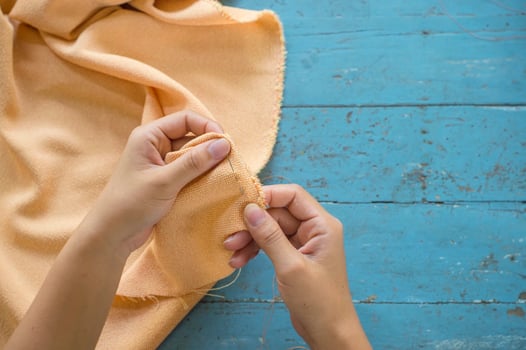 Top view of tailor's hand repair a yellow trousers on blue table background photo