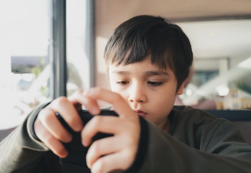 Cenimatic portrait young boy playing game on mobile while waiting for food, Kid sitting in coffee shop sending text to friends, Child playing game online on phone. photo
