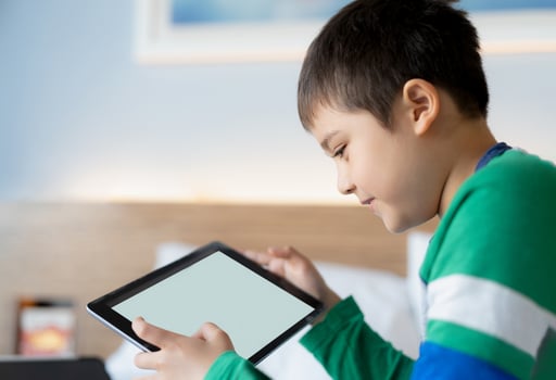 Young boy using tablet playing game on internet with friend, Homeschooling Kid doing homework online by digital pad at home,Child sitting on bed holding touch pad maock up. photo