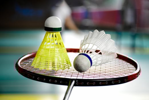 White and yellow plastic badminton shuttlecock and racket with neon light shading on green floor in indoor badminton court, blurred badminton background, copy space. photo