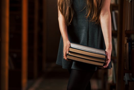 Holds many books in hands. Female student is in library. Conception of education photo