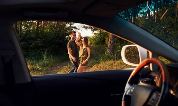 View from the car's interior. Steering wheel, side mirror. Beautiful young couple have a good time in the forest at daytime photo