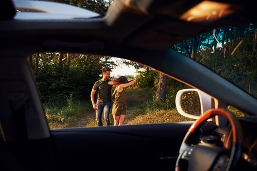 View from the car's interior. Steering wheel, side mirror. Beautiful young couple have a good time in the forest at daytime photo