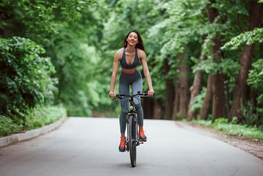 Female cyclist on a bike on asphalt road in the forest at daytime photo