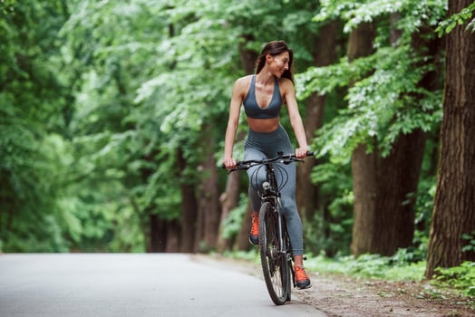With smile on the face. Female cyclist on a bike on asphalt road in the forest at daytime photo
