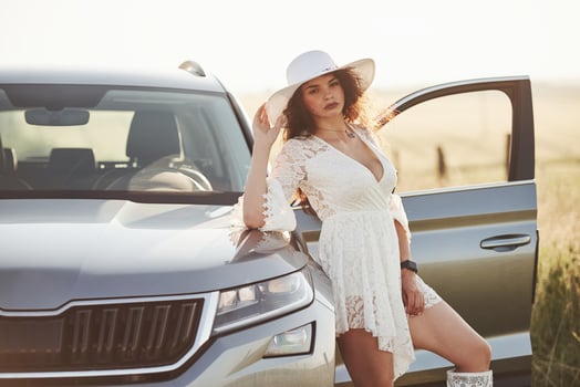 Looks straight into the camera. Girl in white clothes posing near the modern luxury automobile outdoors photo