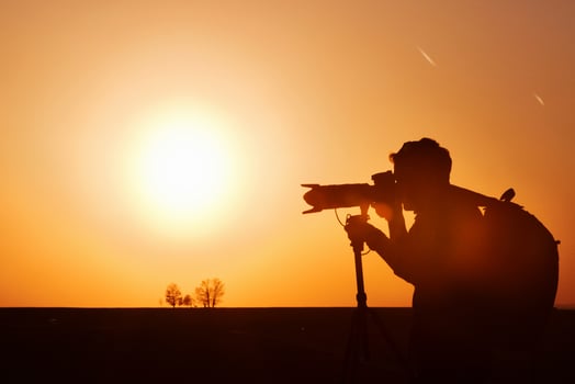 Photographer with professional equipments makes photos. Stands in the field illuminated by sunlight photo