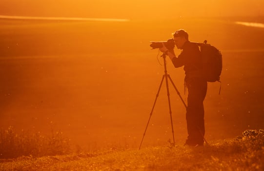 Photographer with professional equipments makes photos. Stands in the field illuminated by sunlight photo