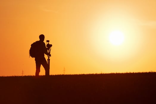 Photographer with professional equipments makes photos. Stands in the field illuminated by sunlight photo