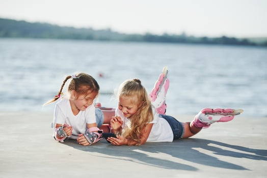 Two little girls with roller skates outdoors near the lake at background photo