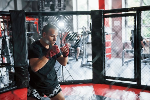 Young boxer in red bandages have exercise. In the gym on the cage photo