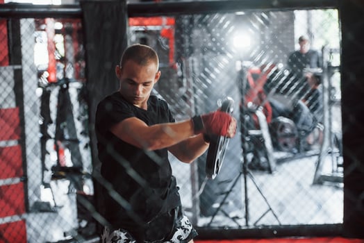 Front view. Young boxer in red bandages have exercise. In the gym on the cage photo