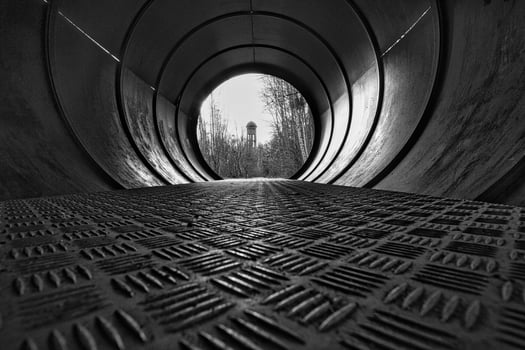 View through a metal pipe. In the background between trees is a water tower. photo