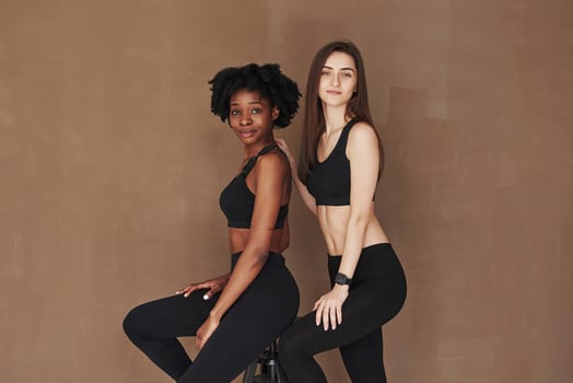 Fashion models. Two multi ethnic female friends stands in the studio with brown background photo