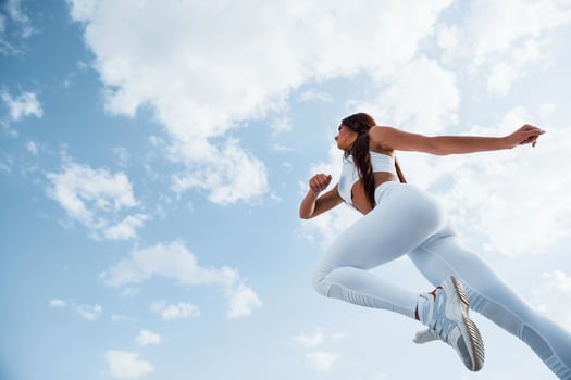 Up in the sky. Female runner in white sportive clothes doing fitness photo