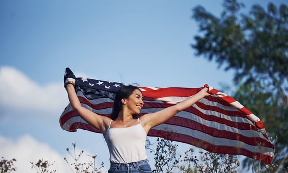 Female patriot runs with USA flag in hands outdoors in the field against blue sky photo