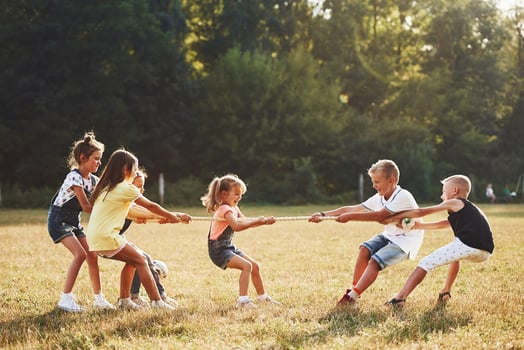 Kids playing tug of war game in the beautiful meadow at sunny day photo