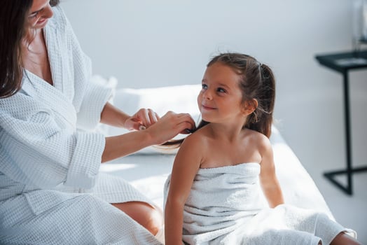 Helping to made hairstyle. Young mother with her daugher have beauty day indoors in white room photo