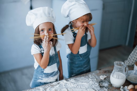 Having fun with spaghetti. Family kids in white chef uniform preparing food on the kitchen photo