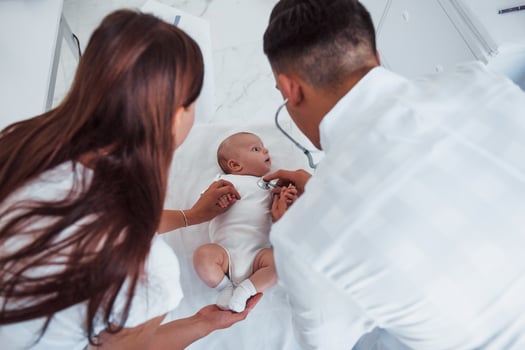 Listening by using stethoscope. Young pediatrician is with little baby in the clinic at daytime photo