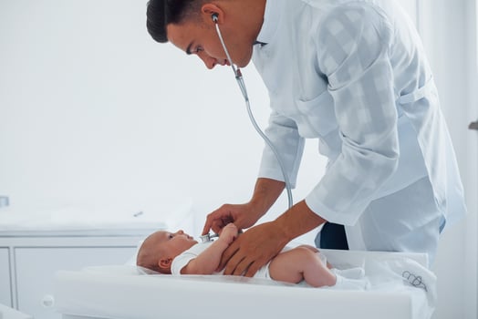Listening by using stethoscope. Young pediatrician is with little baby in the clinic at daytime photo