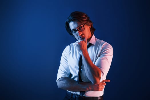 Beautiful man in formal wear and in glasses is in the studio with blue neon lighting photo