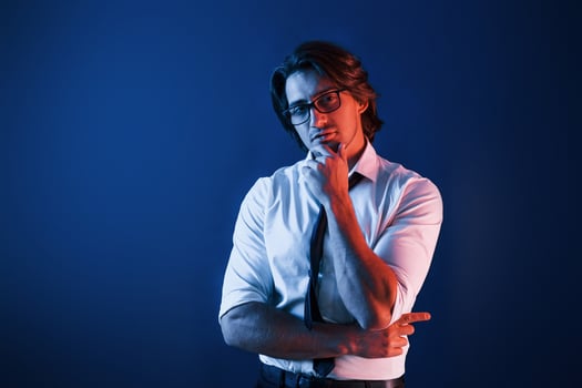 Beautiful man in formal wear and in glasses is in the studio with blue neon lighting photo