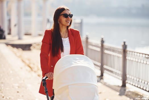 Mother in red coat have a walk with her kid in the pram in the park at autumn time photo