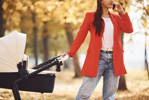 Talking by the phone. Mother in red coat have a walk with her kid in the pram in the park at autumn time photo
