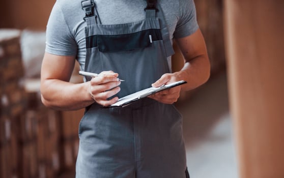 Storage worker in uniform and notepad in hands checks production photo