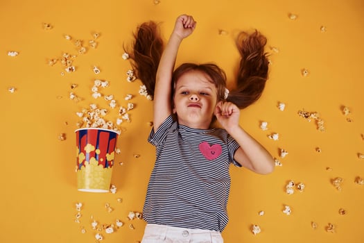 Cute little girl with popcorn lying down on the yellow floor photo