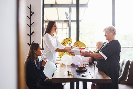Receiving gift box. Senior woman with family and friends celebrating a birthday indoors photo
