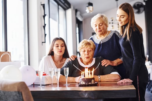 Blowing the candles. Senior woman with family and friends celebrating a birthday indoors photo
