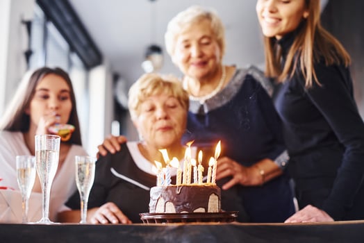 Blowing the candles. Senior woman with family and friends celebrating a birthday indoors photo