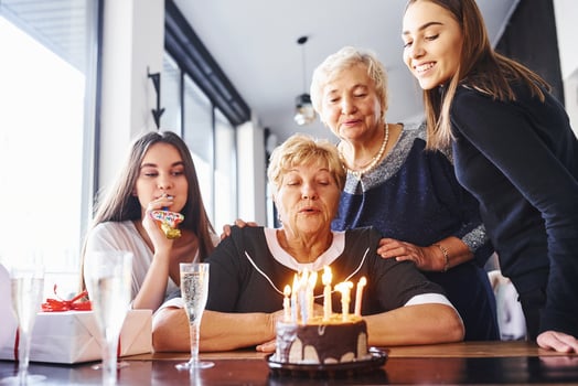 Blowing the candles. Senior woman with family and friends celebrating a birthday indoors photo