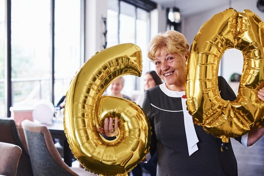 With balloons of number 60 in hands. Senior woman with family and friends celebrating a birthday indoors photo