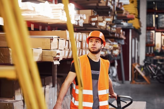 Young male worker in uniform is in the warehouse pushing pallet truck photo