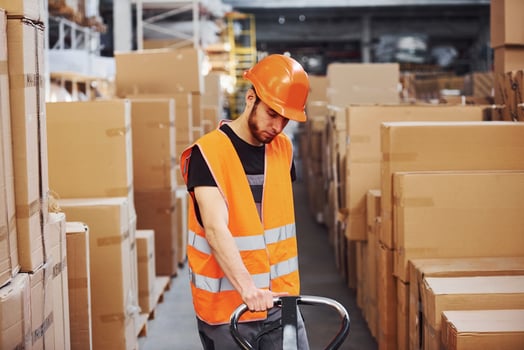 Young male worker in uniform is in the warehouse pushing pallet truck photo