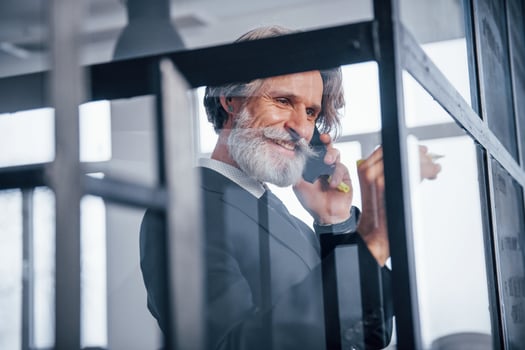 Mature businessman with grey hair and beard in formal clothes have conversation by the phone in the office photo