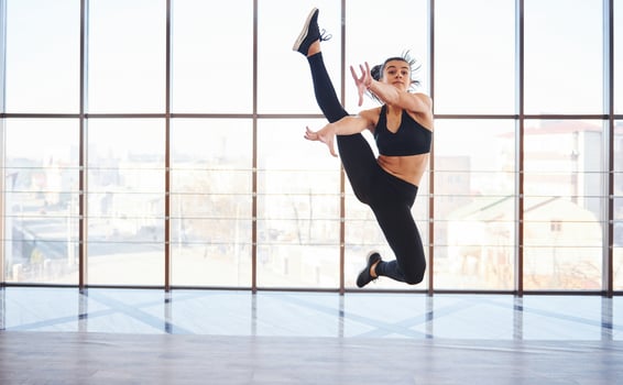 Young sporty woman in sportswear jumping and doing athletic tricks against window in the air photo