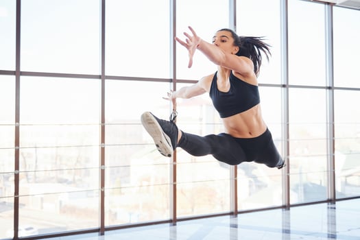 Young sporty woman in sportswear jumping and doing athletic tricks against window in the air photo