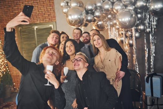 Man taking selfie of his friends that standing in christmas decorated room and celebrating New Year holidays photo