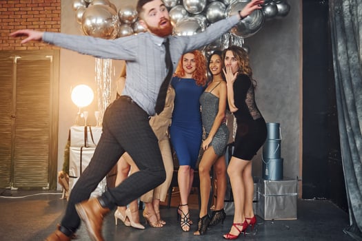 Young women in festive clothes standing indoors of christmas decorated room together and looks at man that have fun doing tricks photo