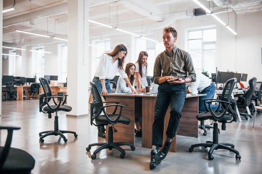 Young male employee in formal clothes standing in the office. Group of people working behind photo