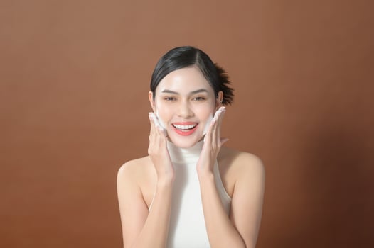 A young woman with beautiful face smiling, washing her face over brown background , beauty skin care concept photo