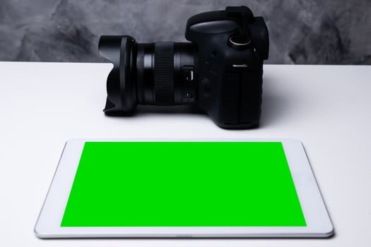 A black digital camera and a blank screen tablet on a table. photo