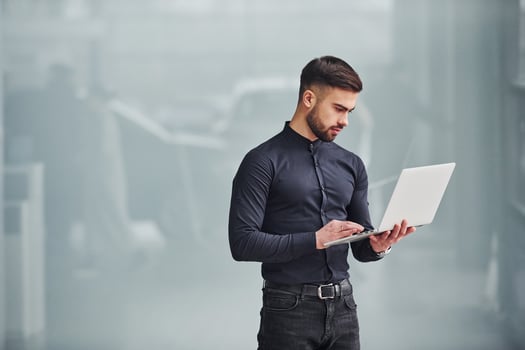 Young bearded guy in elegant clothes standing indoors against grey background photo