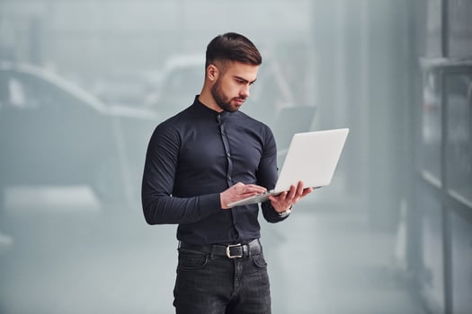 Young bearded guy in elegant clothes standing indoors against grey background photo