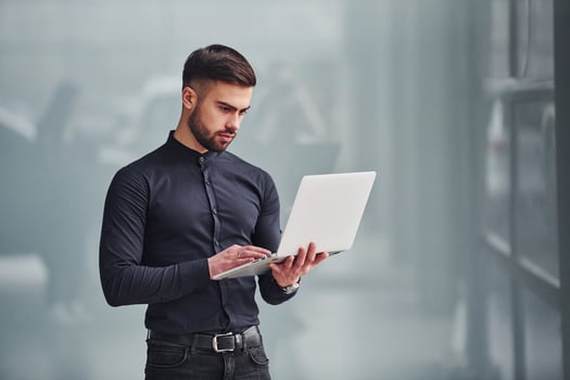 Young bearded guy in elegant clothes standing indoors against grey background photo